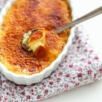 French Crèmes brûlées in a white dish with a spoon that cracked the caramelized top