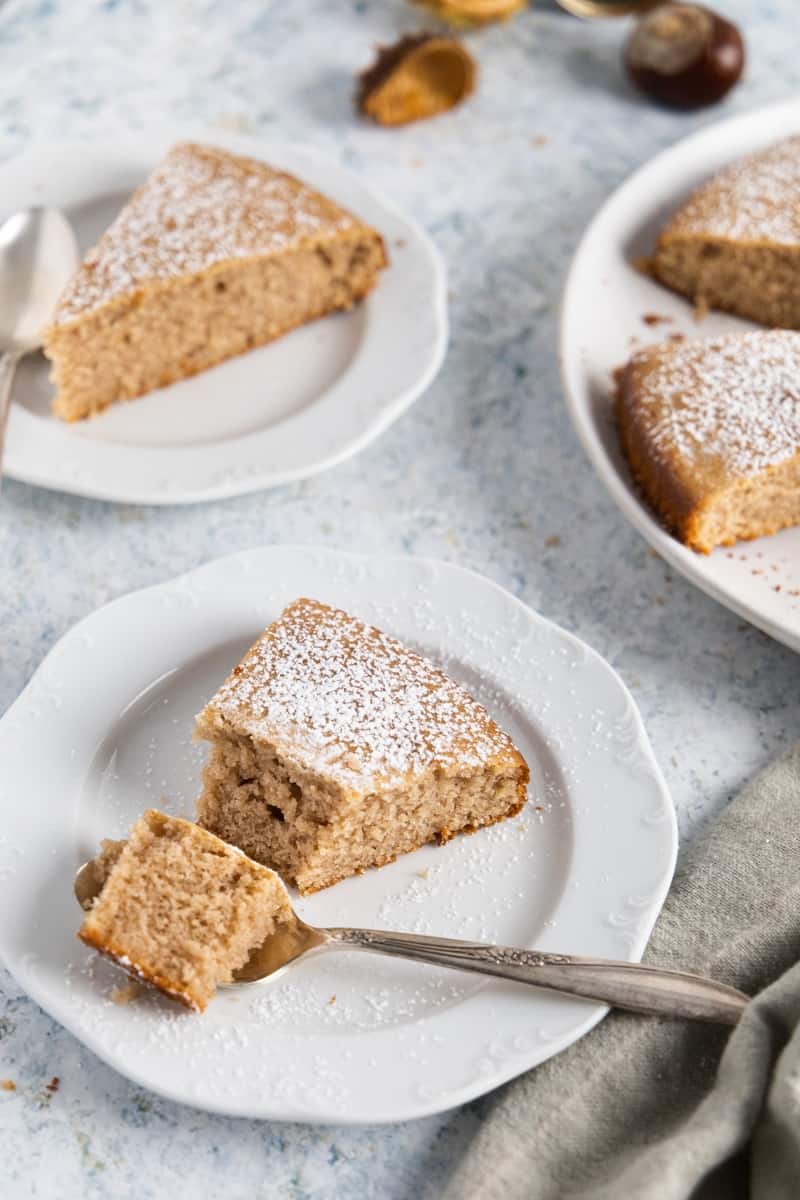 Two small white plates with a slice of chestnut cake each. One has a spoon with some cake in it.