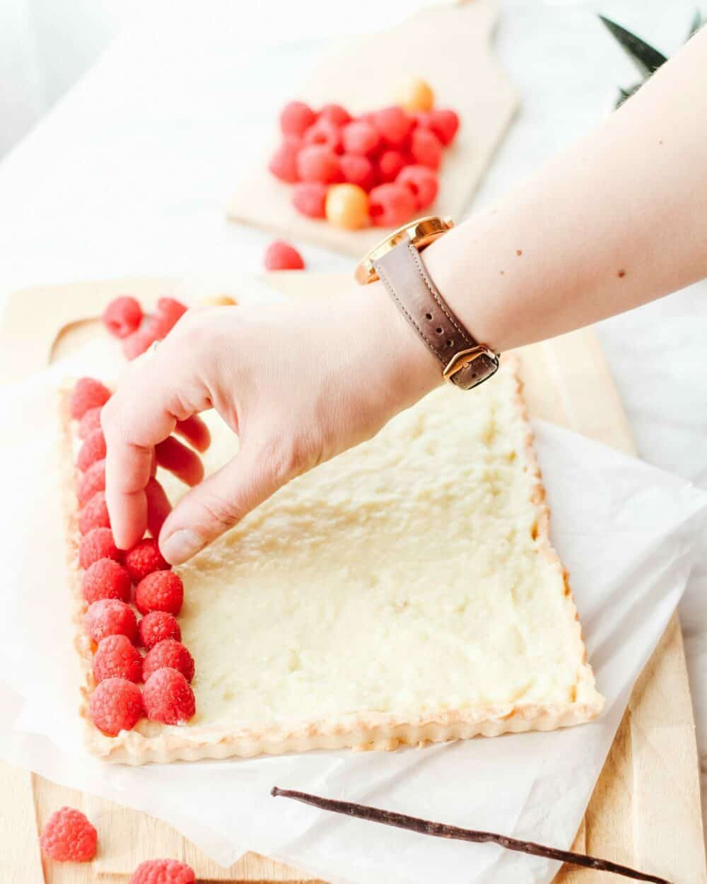 Hand placing raspberries on the french vanilla pastry cream tart