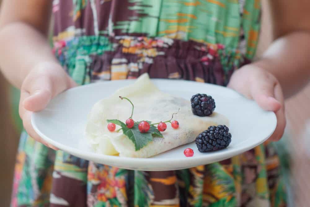 Little girl holding a plate with a French Oat milk creêpes, wearing a summery dress.