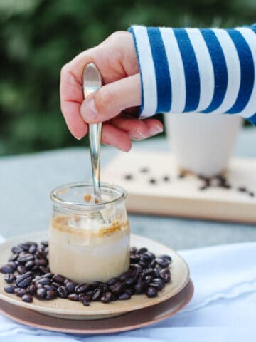 Hand scooping in a coffee pot de creme with whole coffee beans around, stripped sleeve