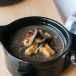 Dairy free sage mushroom soup in 2 individual black cocottes with fall leaves around