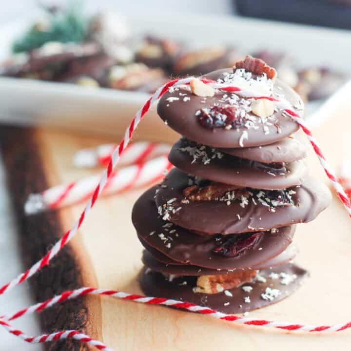 stack of round chocolate bark stacked on a piece of wood and a red and white twine placed on it.