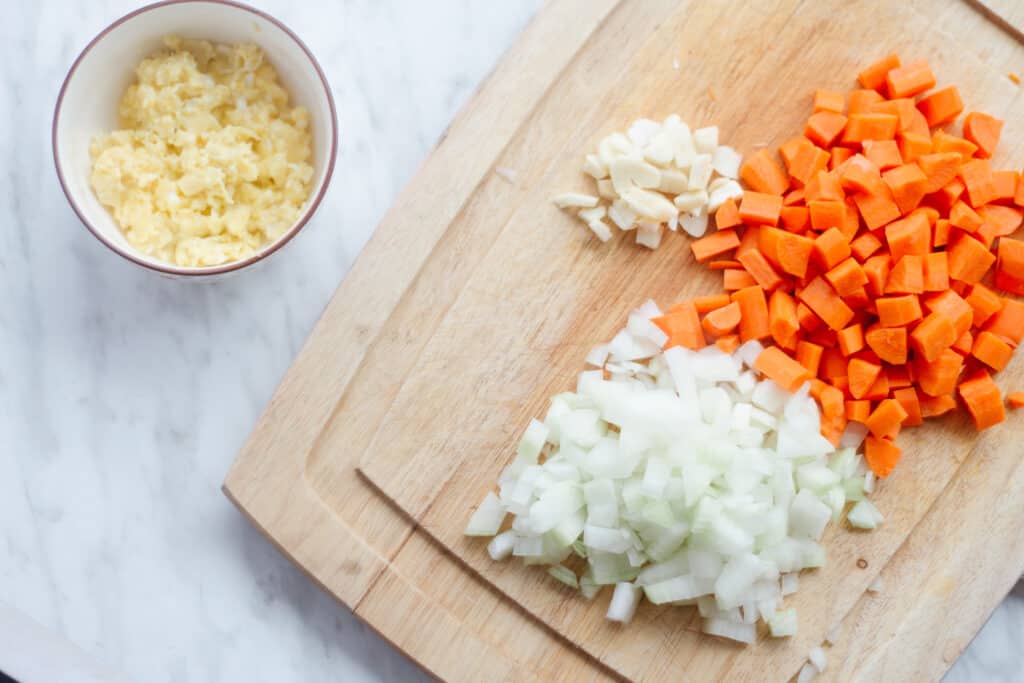 Cooked eggs in a bowl and a cutting board with carrots, onions and garlic