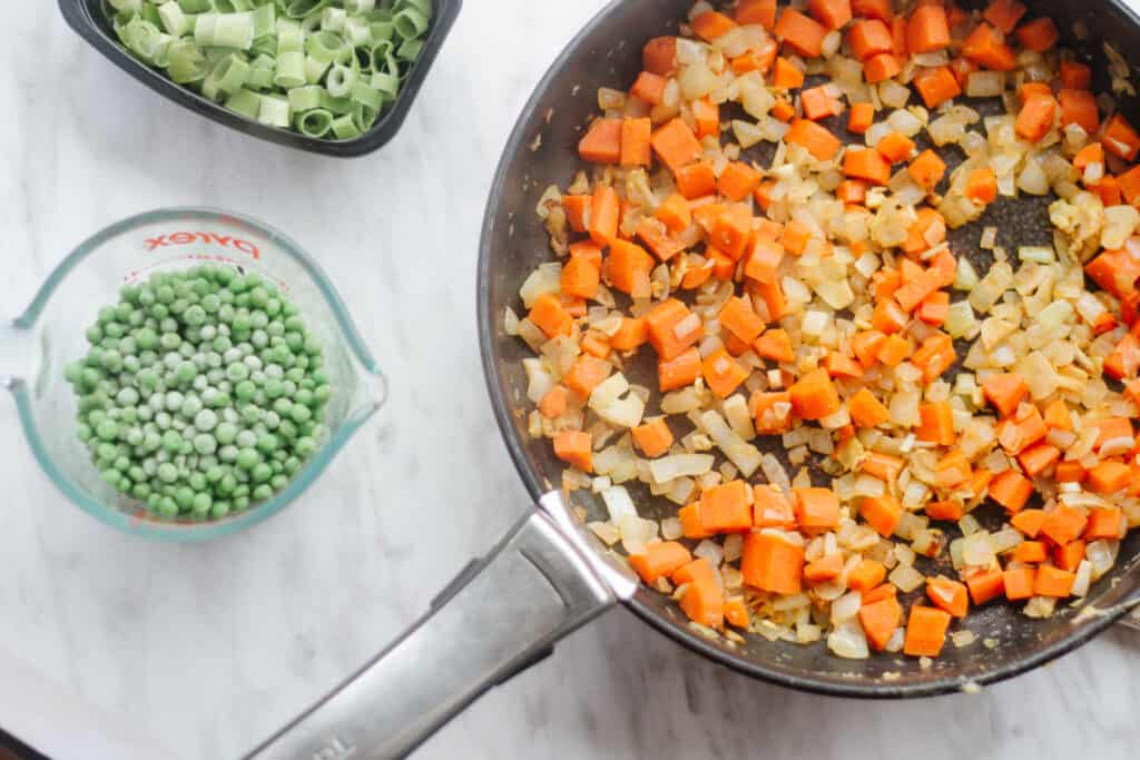 Cooked carrots, onion, garlic in a pan and peas and scallions on the side