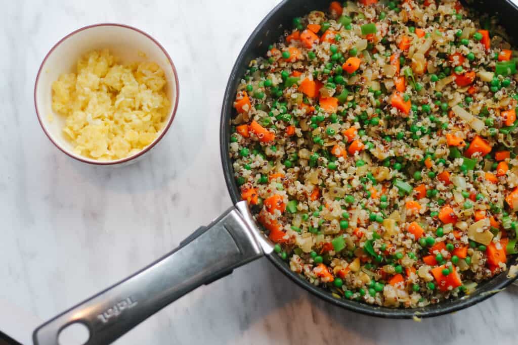 Quinoa Fried Rice: Cooked quinoa and veggies in a pan and cooked eggs on the side in a bowl