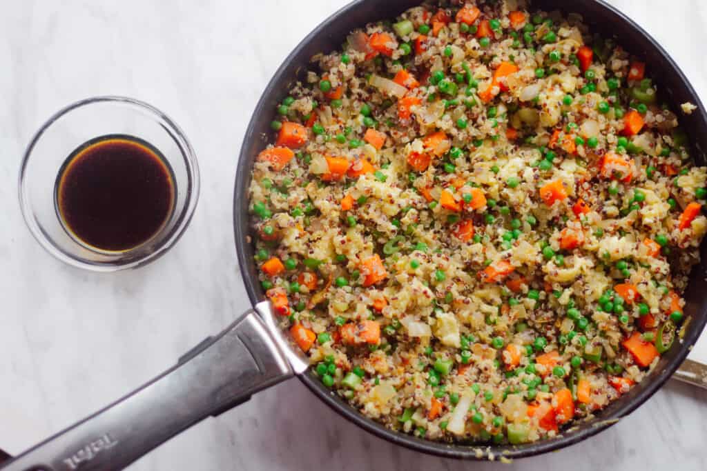 Cooked quinoa fried rice in a bowl and sauce on the side