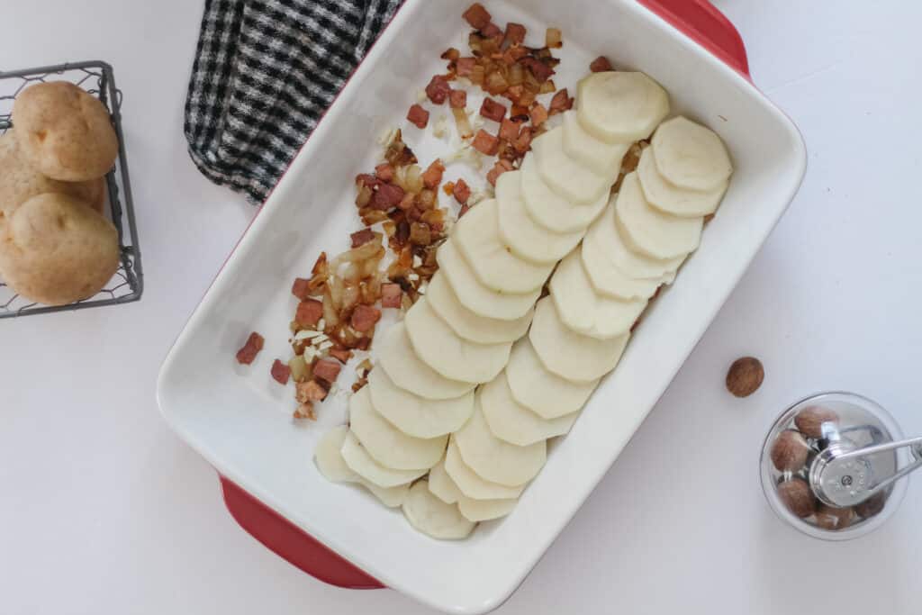 Building the scalloped potatoes dish:Thinly sliced potatoes on ham and onion
