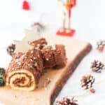 Chocolate Yule log on a a piece of wood. Pine cones around and a nutcracker in the back.