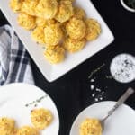 Duchess potatoes piled in a rectangle dish and small round plates with some served, rustic serving spoon. Black background.