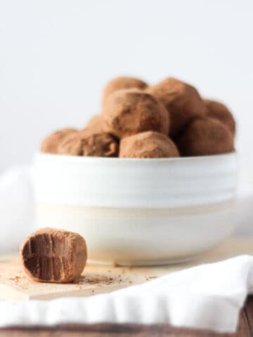Bowl of homemade truffles in a white bowl with one bitten on the side