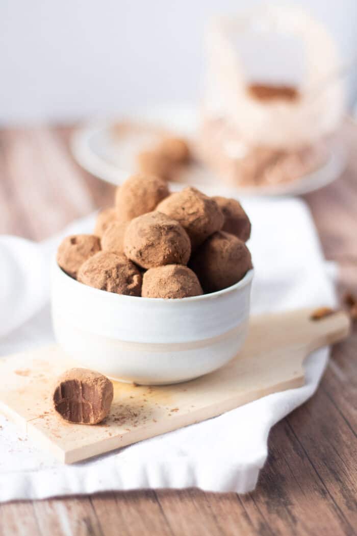 Bowl of homemade truffles in a white bowl with one bitten on the side