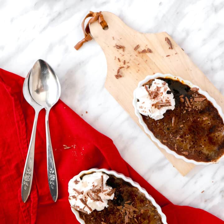 Top view of 2 chocolate cremes brulees, 2 spoons and a red dish towel.