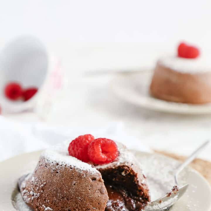 Side view of a lava cake cut in the middle with gooey chocolate. Raspberries around.