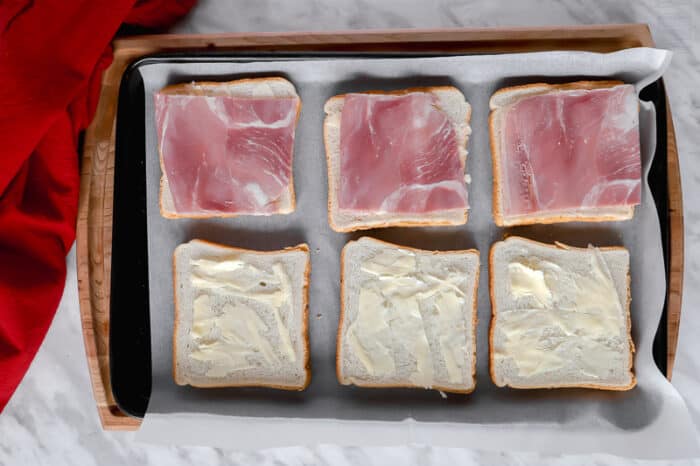 Top view of buttered bread and ham on a baking sheet