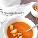 Close up of a carrot ginger soup in a white bowl with some croutons on top. Another bowl in the background with a white napkin.