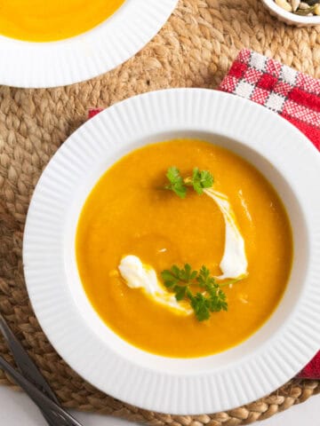 orange soup in a white bowl with a dollop of white cream and parsley as garnish.