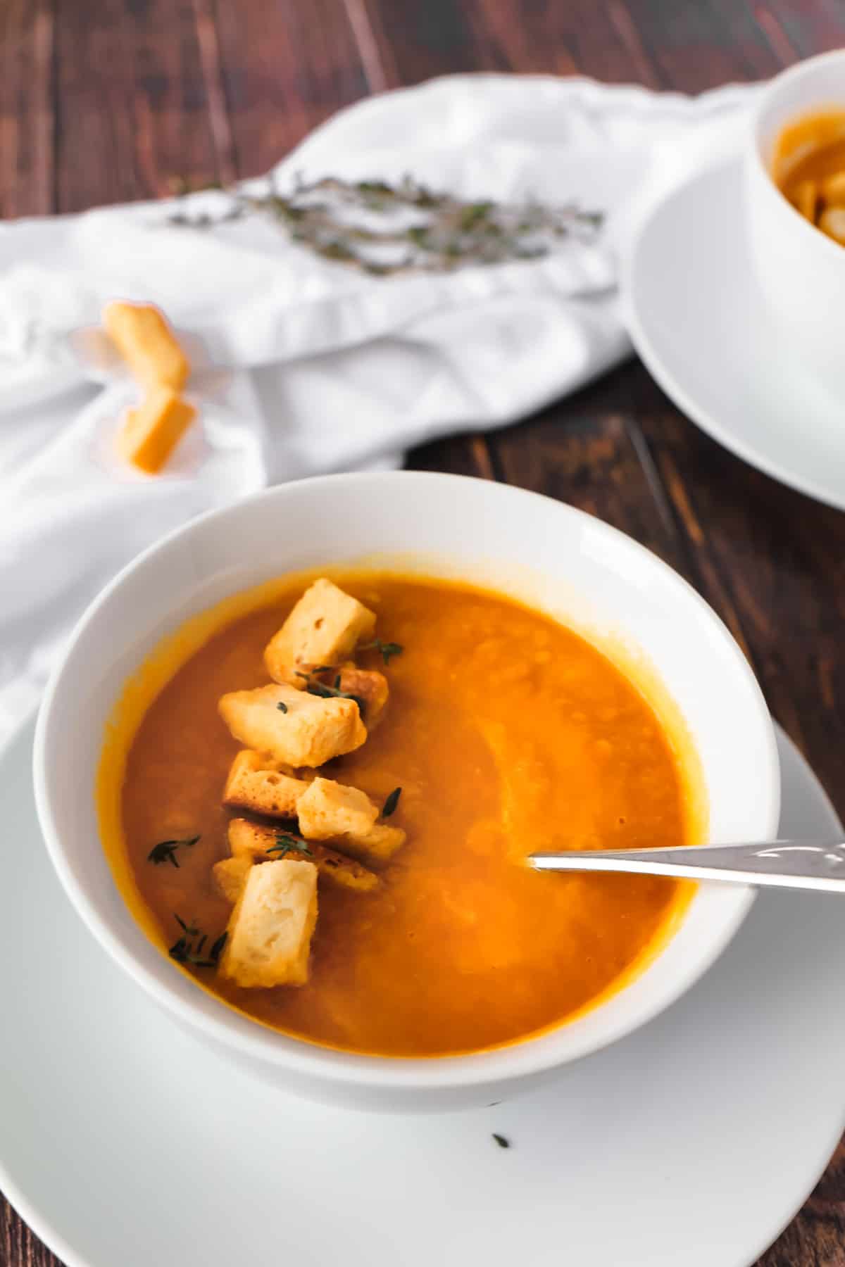 white bowl with an orange soup and some croutons on top and a spoon in it. 