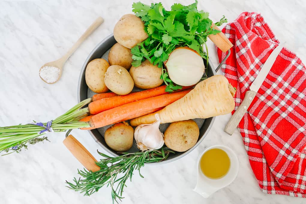 Round metal tray of vegetable with a red tea towel on the side and a wooden knife.