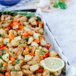 Side view of roasted carrots and potatoes in a baking sheet with a slice of lemon on the corner.