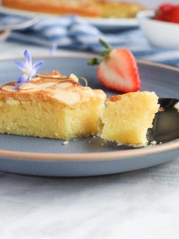 Slice of almond cake in a blue plate with a strawberry in the bake.