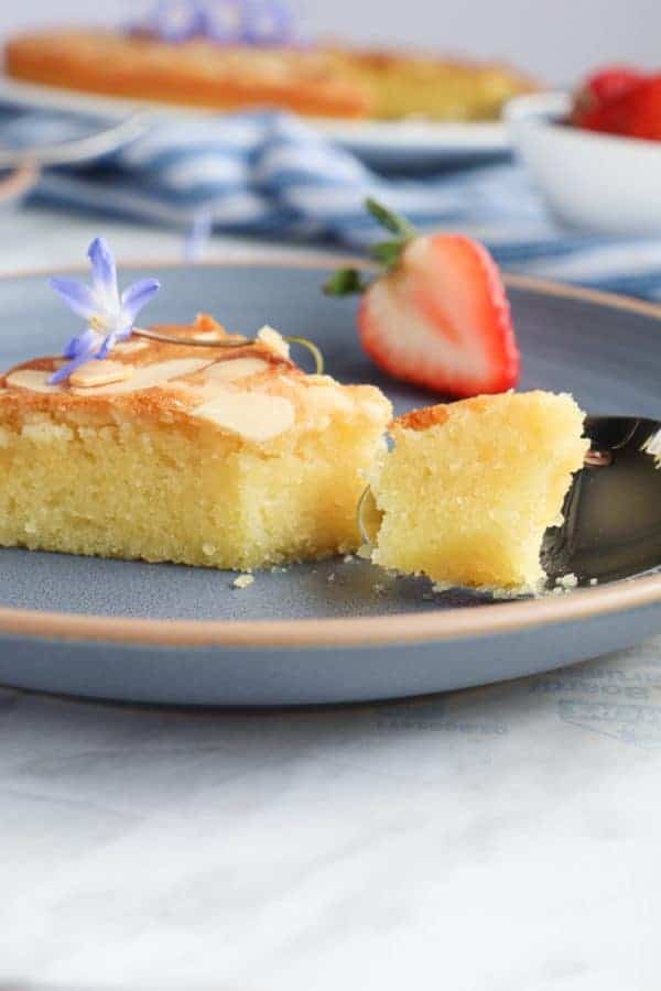 Slice of almond cake in a blue plate with a strawberry in the bake.