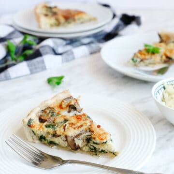 45 angle of 3 white plates with a slice of spinach quiche, partial view of quiche dish and cheese ramekin