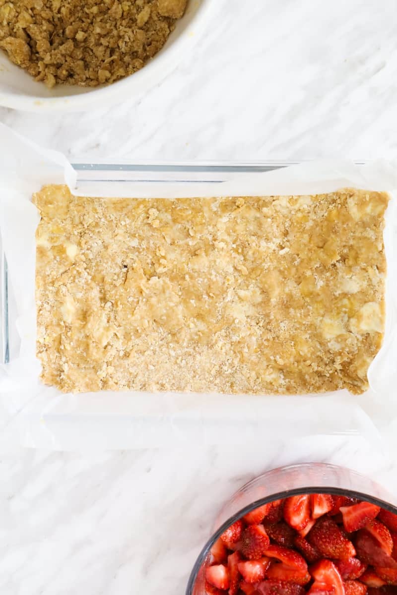 top view of a rectangular oven dish with shortbread dough and a bowl of strawberries on the side