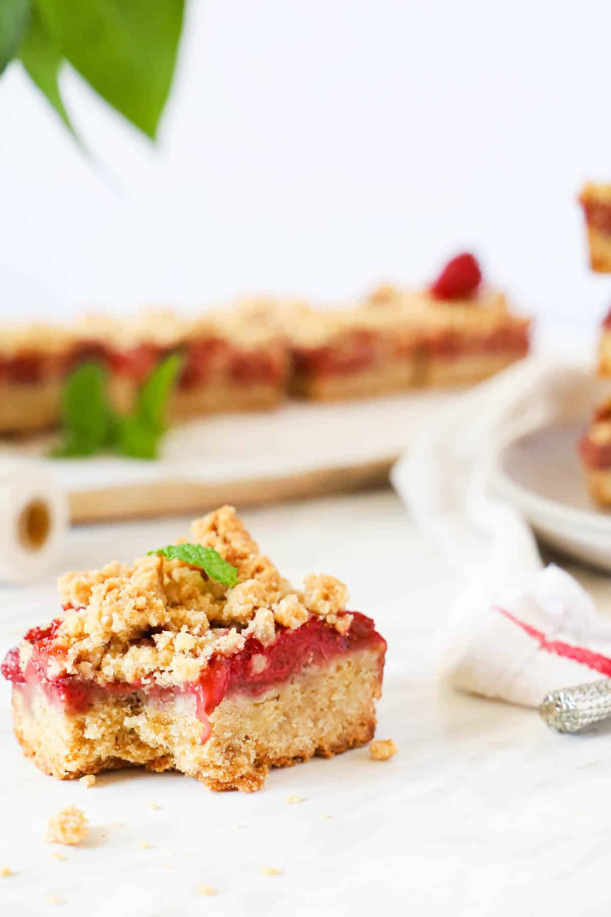 bitten strawberry crumble bar on a small plate on an old book. A small leaf of mint is on top.