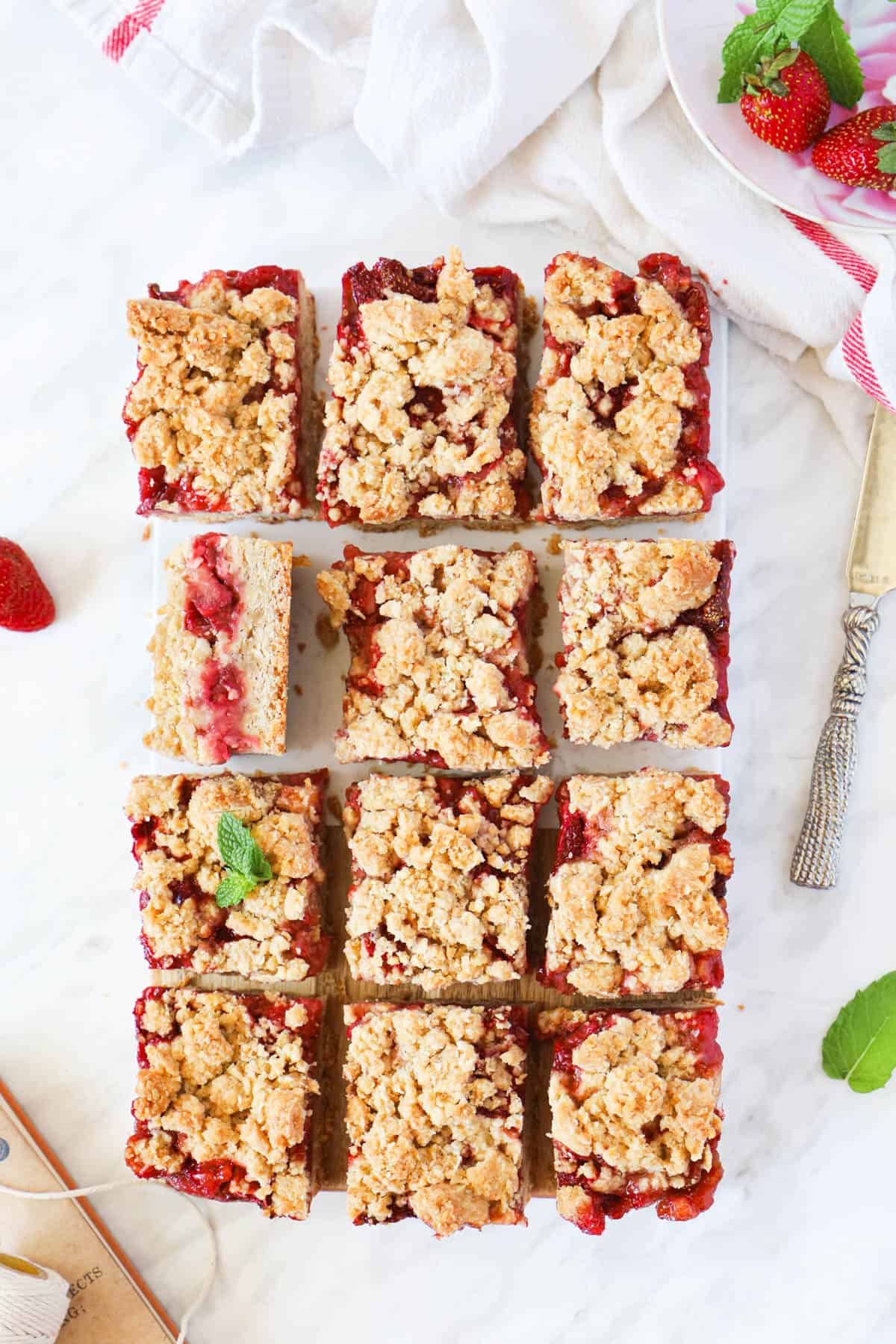 squares of the strawberry crumble bar, ramekin of fresh strawberries on the side. and an old book.