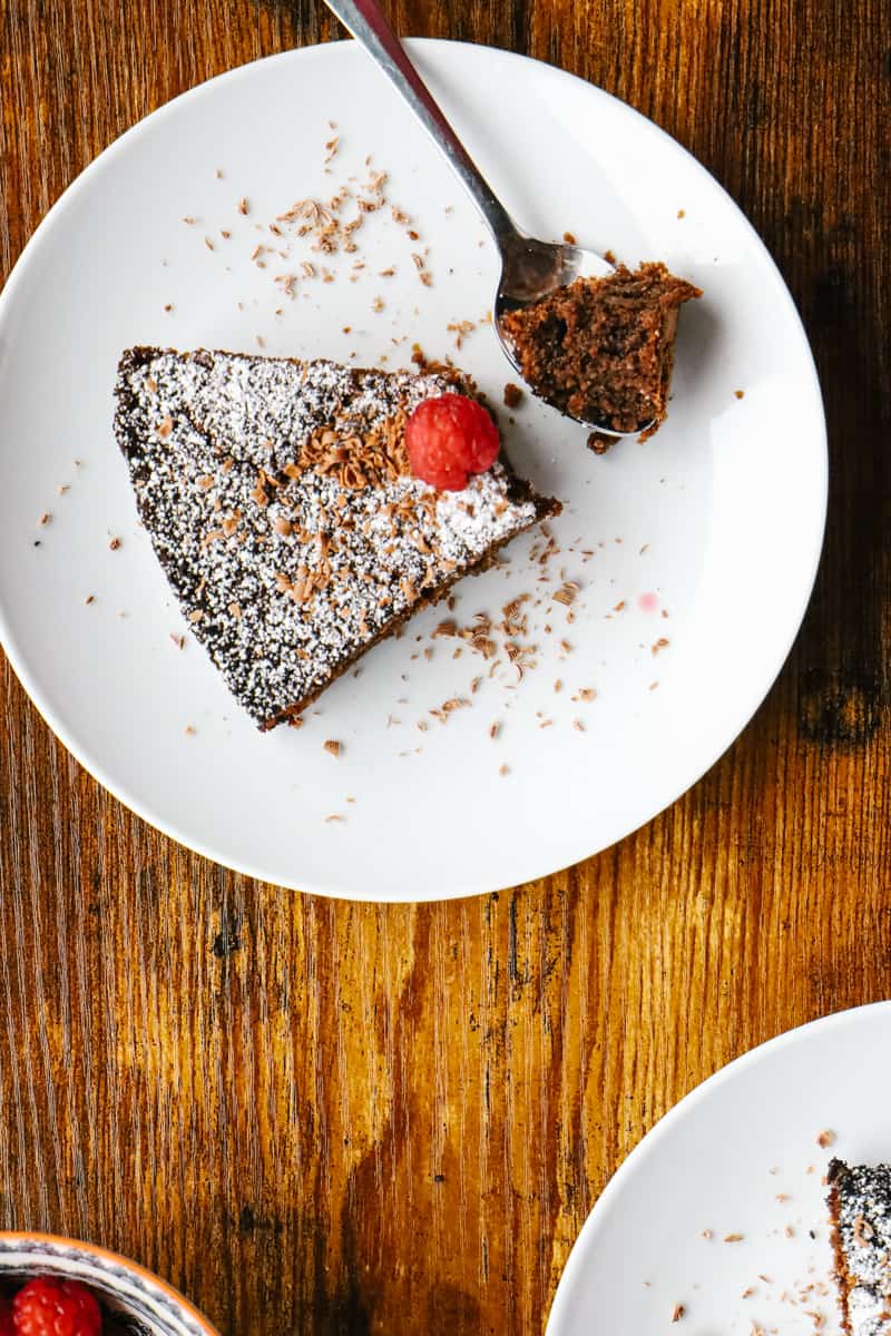 a slice of chocolate cake with icing sugar and a raspberry on it. A piece is taken in spoon. 