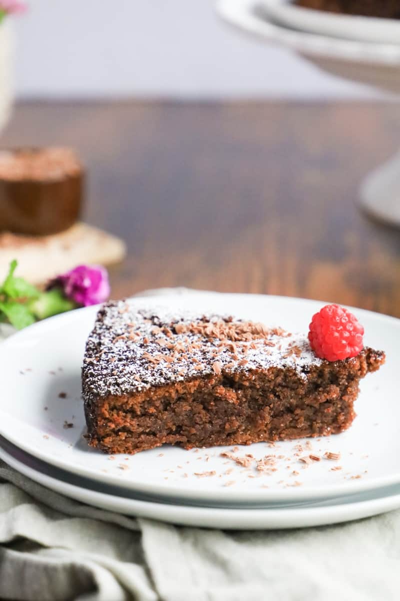 side view of a moist chocolate cake with a raspberry on a top in a white plate.