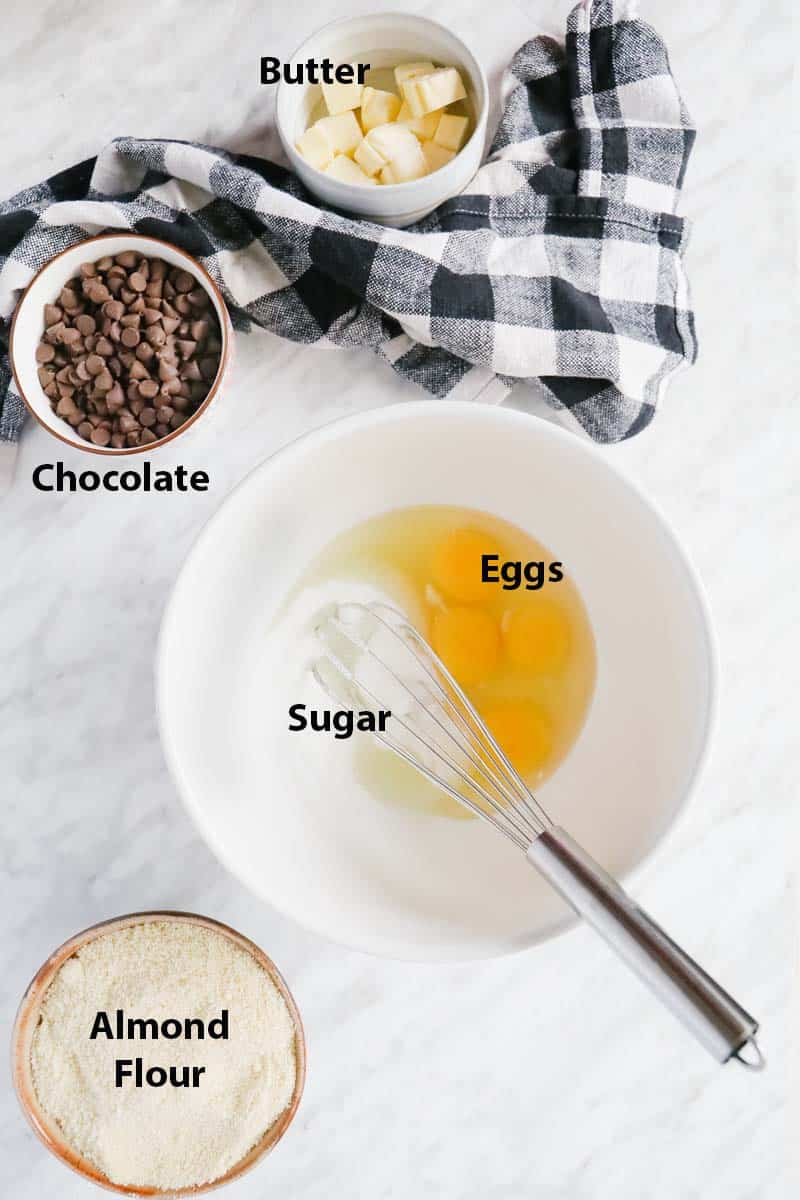 ingredients, eggs and sugar in a white bowl with a whisk. Chocolate chips, butter and almond flour in separate ramekins.