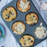 Top view of almond muffins cooked in a muffin tin. Ripe bananas on the side and egg shells.