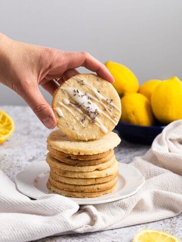 side view of a stack of lemon lavender cookies with one being held with a hand, it has a drizzle on it.