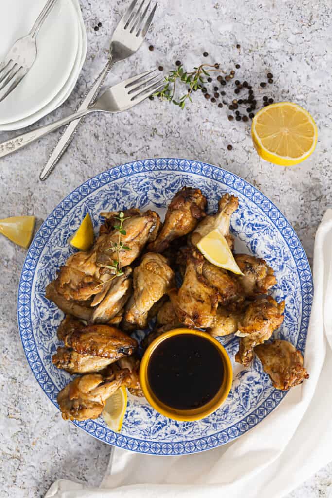 Top view of a blue plate with air fryer lemon pepper wings and fresh lemon on the side and grains of pepper
