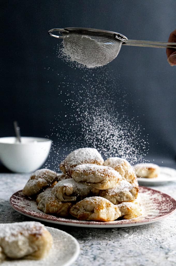 Side view of a pile of pastelitos de guayaba on a pink plate with sugar dusted on top