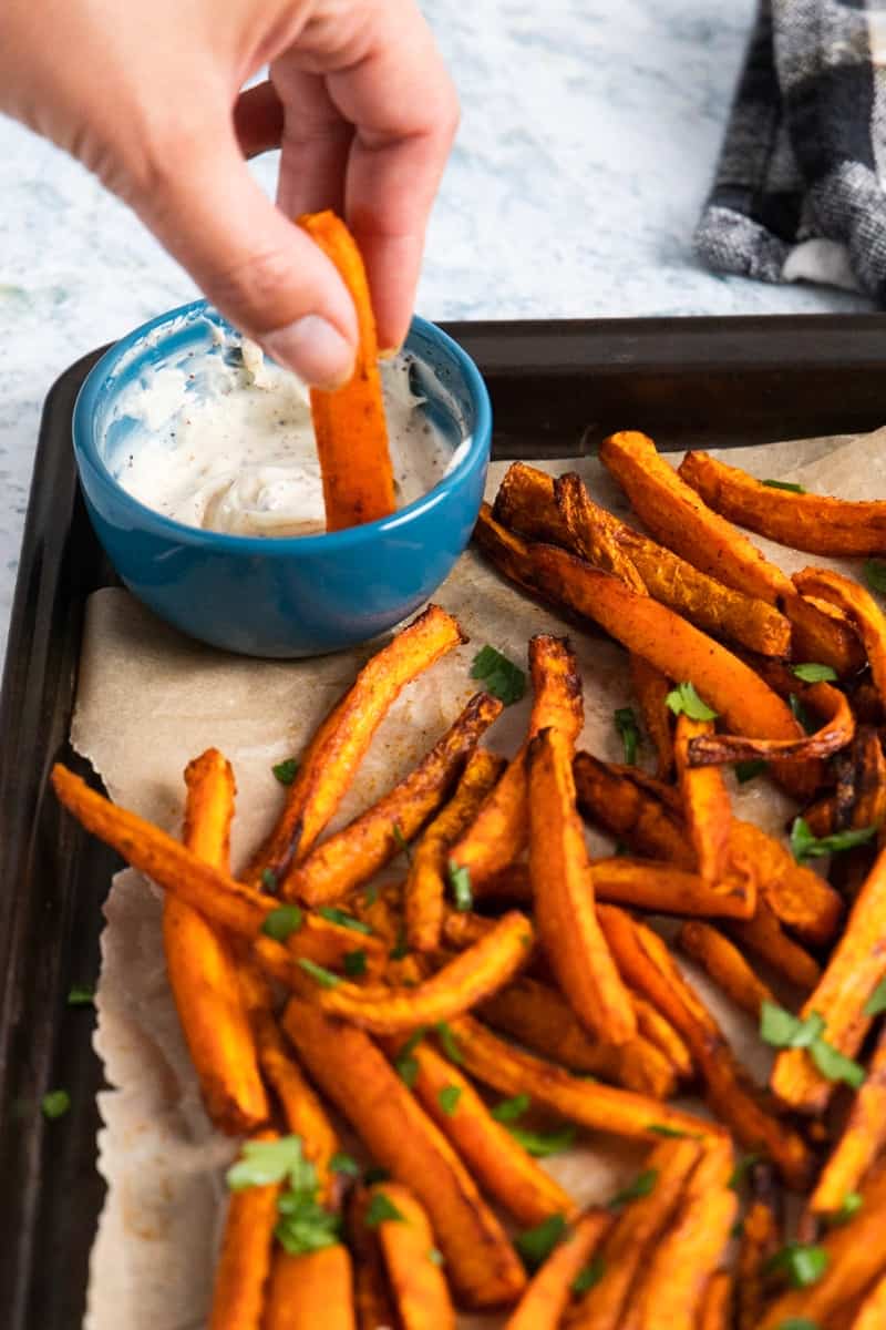 hand holding a carrot fry and dipping in a dip in a blue mini bowl