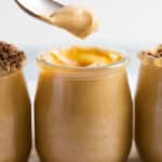 close up of a class jar with dulce de leche mousse and a spoon with some on it.