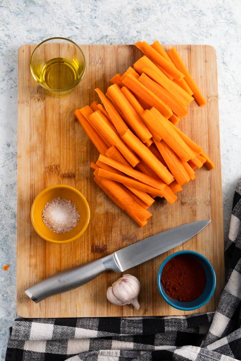 top view of a chopping board with carrot sticks, salt, olive oil and a silver knife.