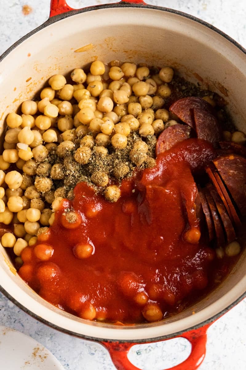 Top view of a large pot with chickpeas, tomato sauce, chorizo and oregano