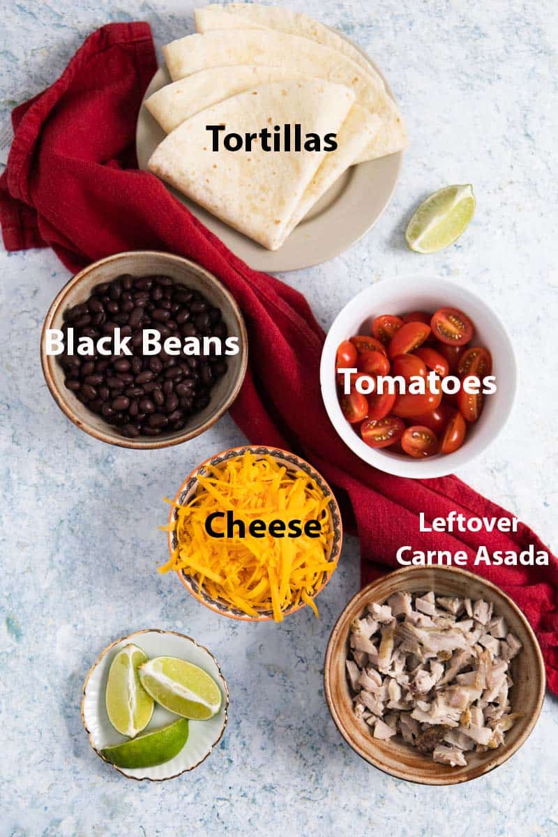 top view of bowls with ingredients, carne asada, cheese, tomatoes, black beans and tortillas