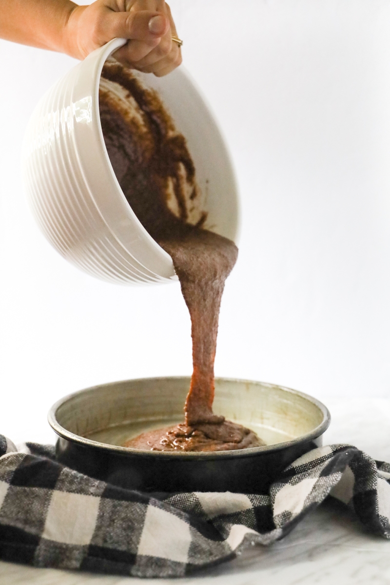 chocolate cake batter being poured in a round baking dish