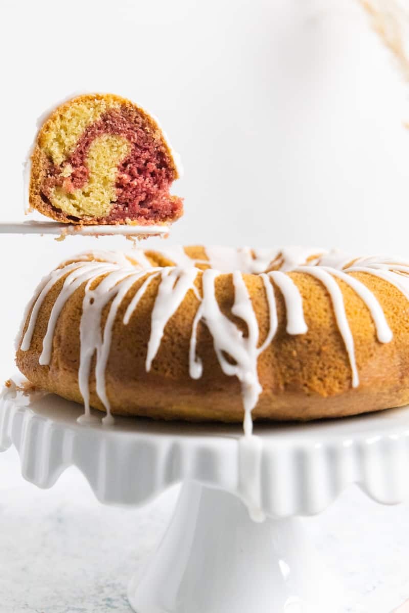 Side view of a Bundt cake with a drizzle and a sliced of cake where you can see the moist marble almond cake and red velvet
