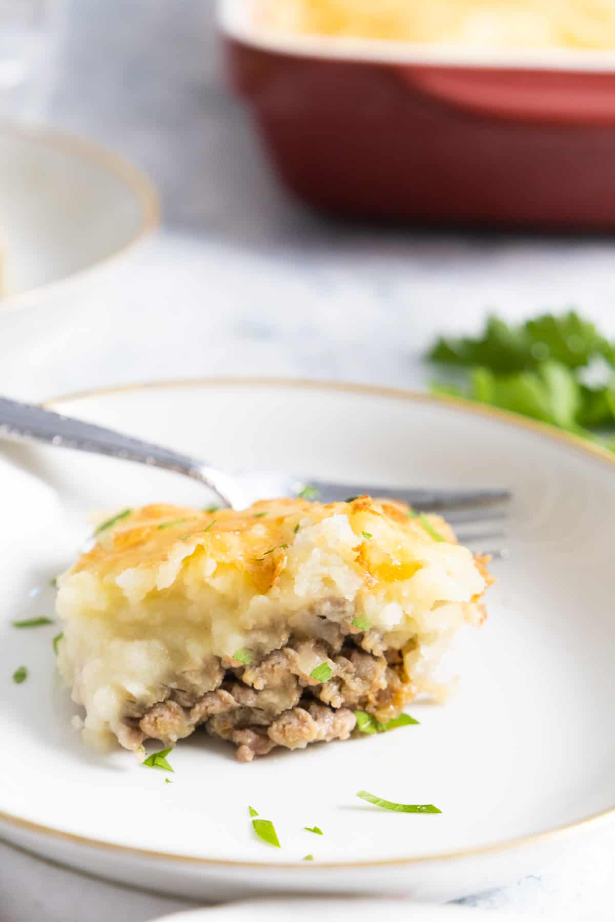 portion of shepherd's pie in a white plate with a golden rim with a fork.