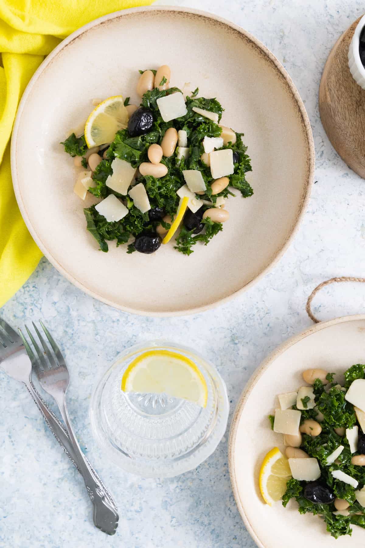one plate with kale salad, a yellow tea towel on the top left corner and another plate on the bottom right corner.