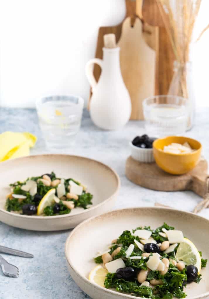 2 beige plates with some salad in the centre of each, in the background, some small wood chopping board, a ramekin with parmesan.