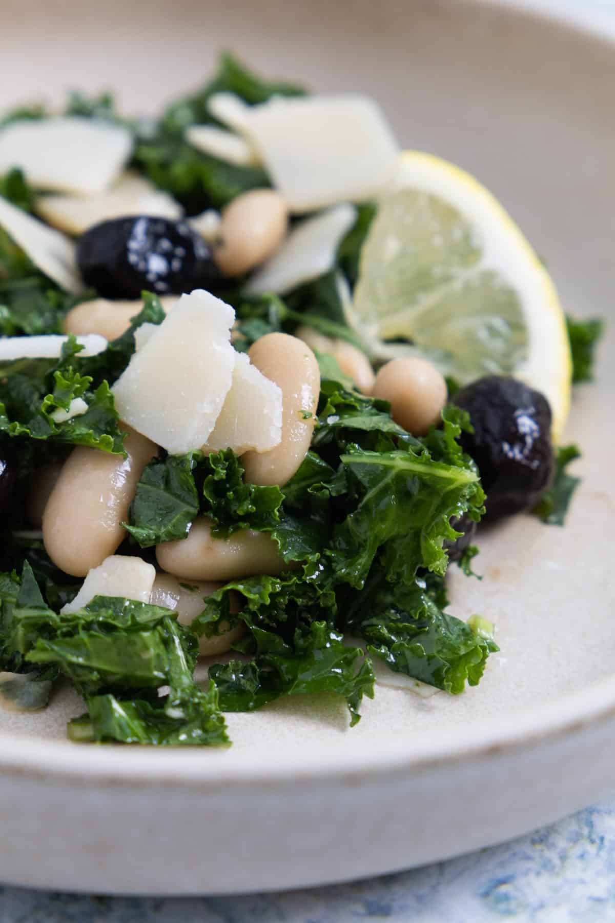 close up of a kale salad with shaved parmesan cheese, kalamata olives and white beans. 