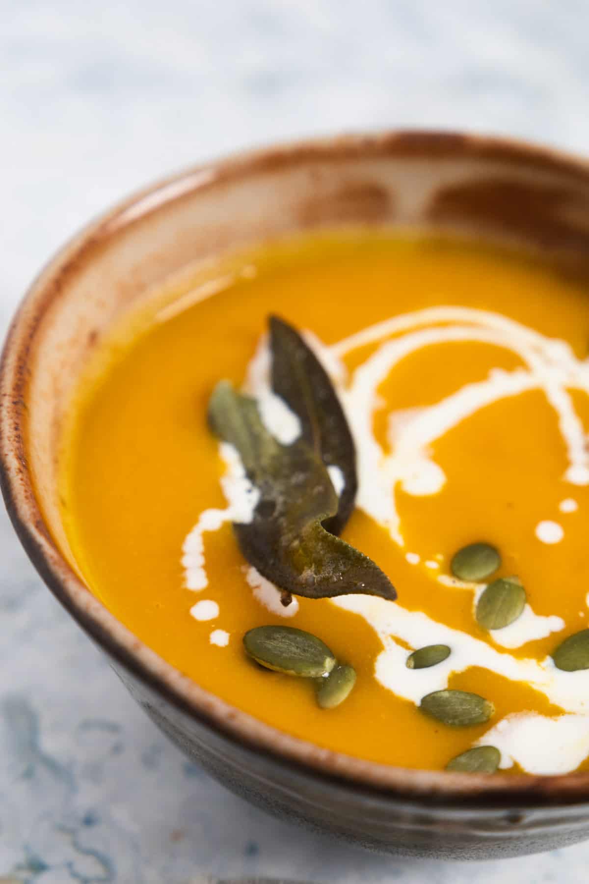 partial view of a bowl of butternut squash soup with a drizzle of cream and pumpkin seeds on it. 