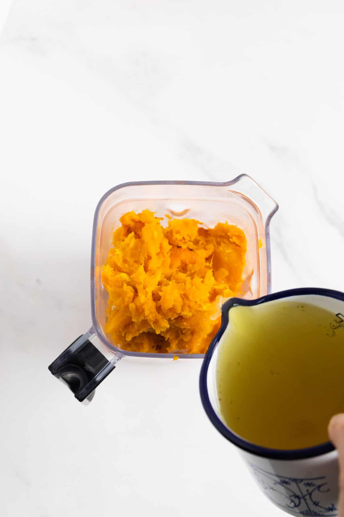 broth poured in a blender where there is an orange purée. 